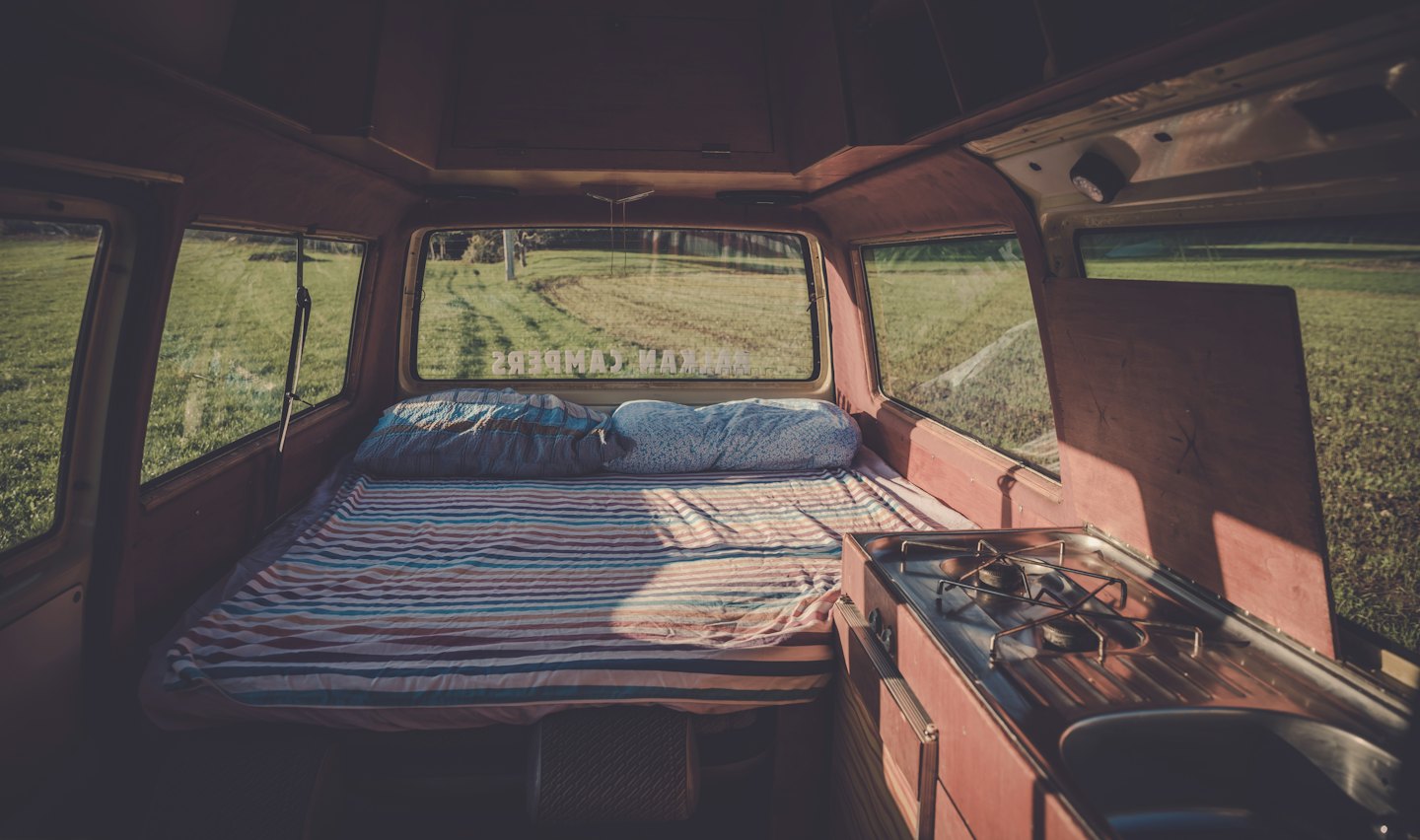 Gemütlicher Camper-Innenraum mit Bett und Küche, Blick auf ein Feld.