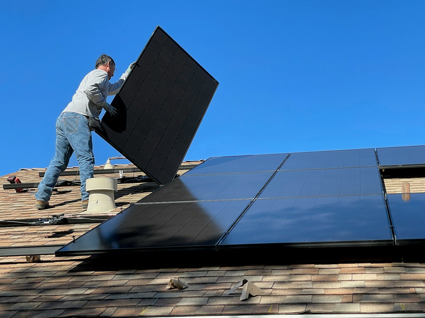 Techniker installiert Solarmodul auf Schrägdach unter blauem Himmel.